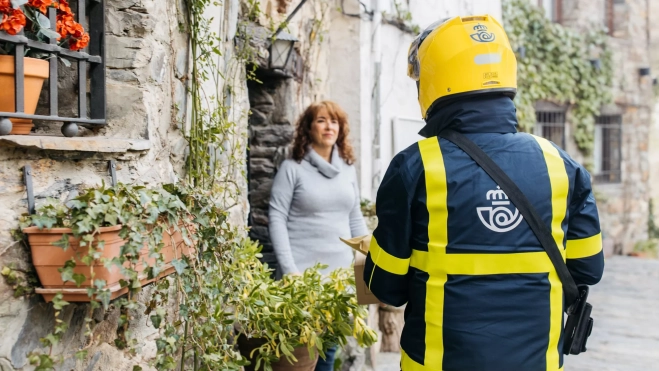 Un trabajador de correos entrega dinero a una mujer en un pueblo / CAIXABANK Un trabajador de correos entrega dinero a una mujer en un pueblo / CAIXABANK