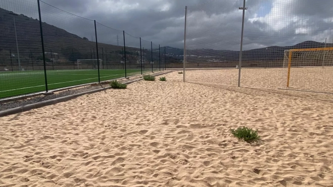 Una mata de hierba crece en la cancha de vóley playa. / AH